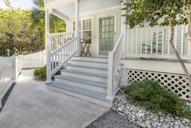 view of exterior entry featuring covered porch and fence