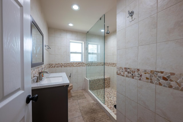 bathroom with a tile shower, tile walls, tile patterned flooring, vanity, and toilet