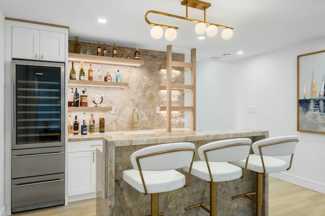 bar featuring wine cooler, white cabinets, light wood-type flooring, and decorative light fixtures