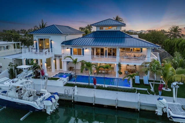 back house at dusk featuring a swimming pool with hot tub, a patio area, and a balcony