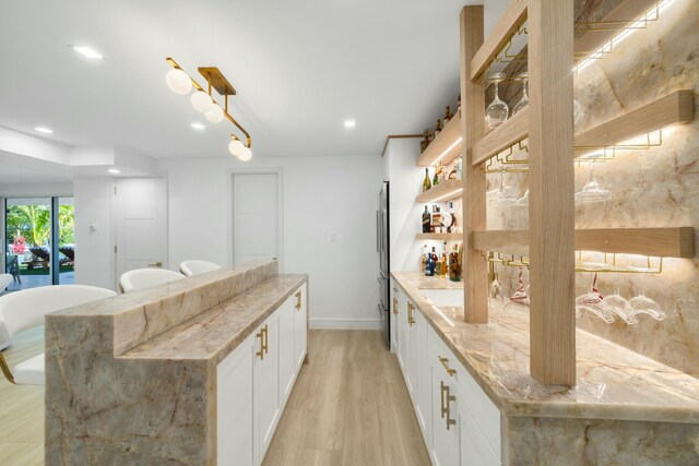 kitchen with stainless steel refrigerator, white cabinetry, a center island, light stone counters, and light hardwood / wood-style flooring