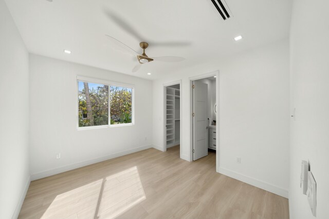 unfurnished bedroom featuring ceiling fan, a spacious closet, a closet, and light hardwood / wood-style flooring