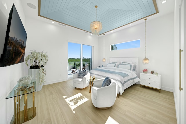 bedroom featuring access to exterior, light hardwood / wood-style floors, a raised ceiling, and a chandelier