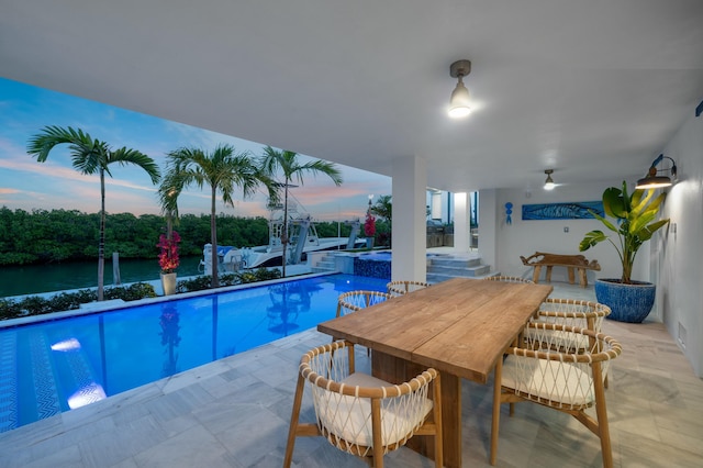 pool at dusk featuring a patio, an in ground hot tub, a water view, and exterior bar