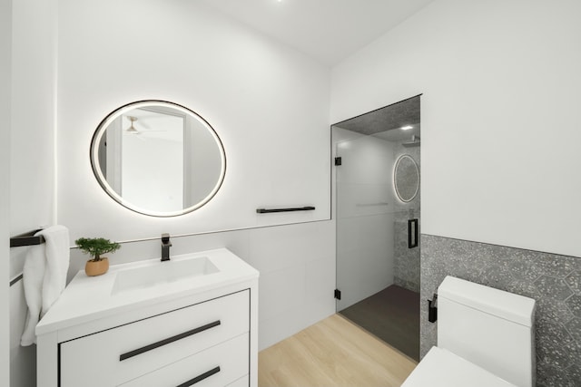 bathroom featuring hardwood / wood-style flooring, tile walls, vanity, toilet, and walk in shower