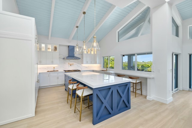 kitchen featuring a center island, a kitchen breakfast bar, pendant lighting, wall chimney range hood, and white cabinets