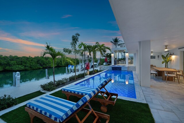 pool at dusk with a patio area, an in ground hot tub, and a water view