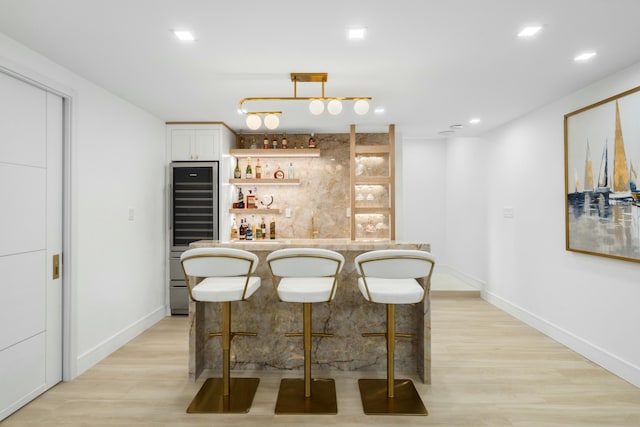 bar featuring white cabinetry, pendant lighting, and light hardwood / wood-style flooring