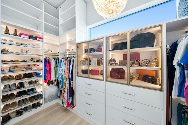 walk in closet with an inviting chandelier and light hardwood / wood-style flooring