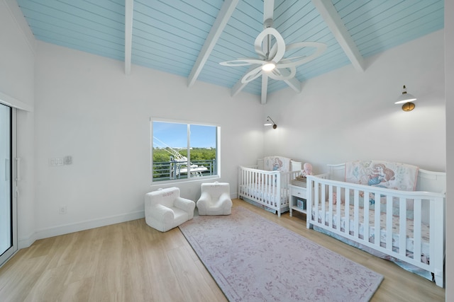 bedroom featuring a crib, light hardwood / wood-style flooring, lofted ceiling with beams, and wooden ceiling