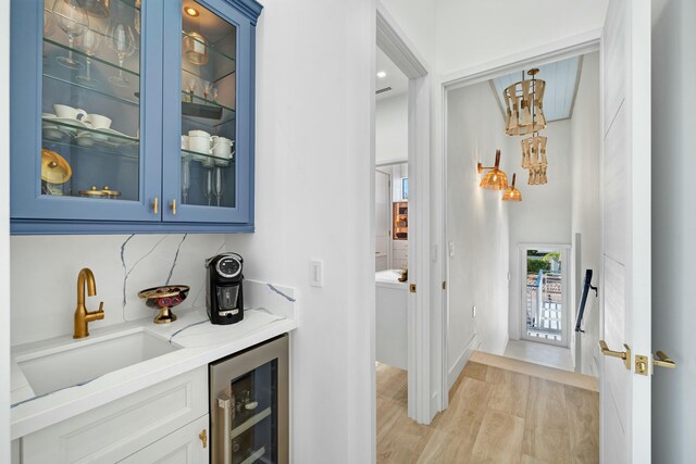 bar with sink, white cabinets, beverage cooler, light hardwood / wood-style floors, and blue cabinetry