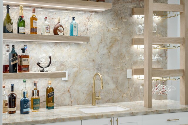 bar with white cabinetry, sink, tasteful backsplash, and light stone countertops