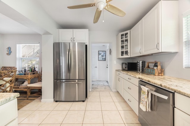 kitchen with light tile patterned floors, ceiling fan, appliances with stainless steel finishes, light stone counters, and white cabinets