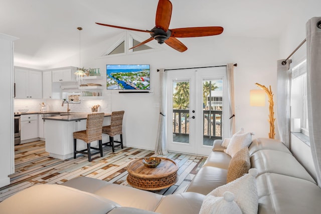 living room with sink, ceiling fan, light hardwood / wood-style floors, vaulted ceiling, and french doors