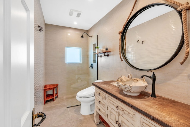 bathroom with toilet, tile walls, a tile shower, vanity, and tile patterned flooring