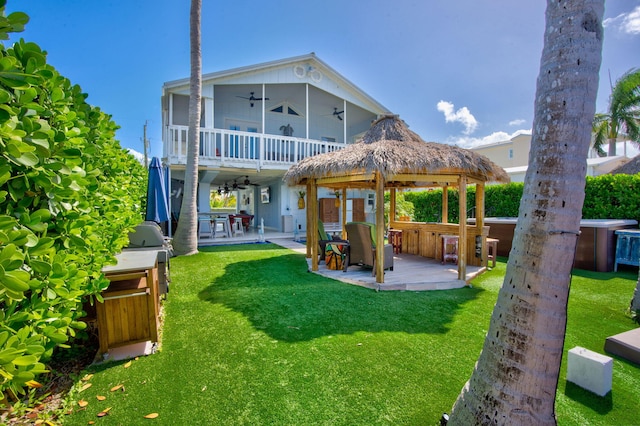 back of house with ceiling fan, a yard, a patio area, a hot tub, and a bar