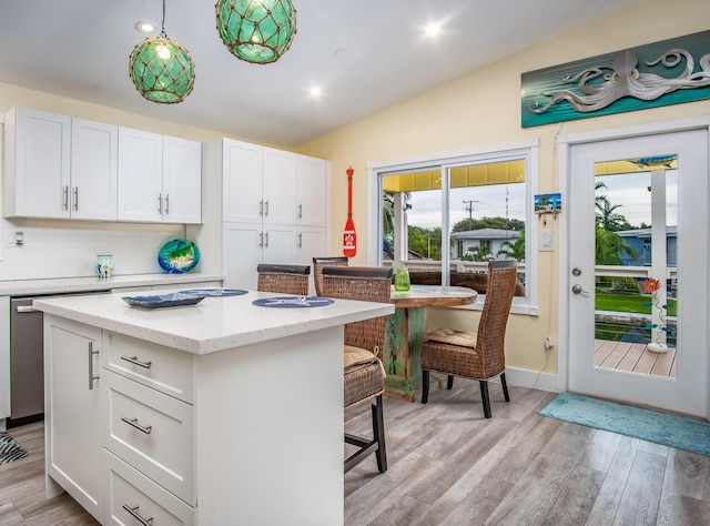 kitchen featuring a breakfast bar, white cabinetry, hanging light fixtures, a center island, and vaulted ceiling