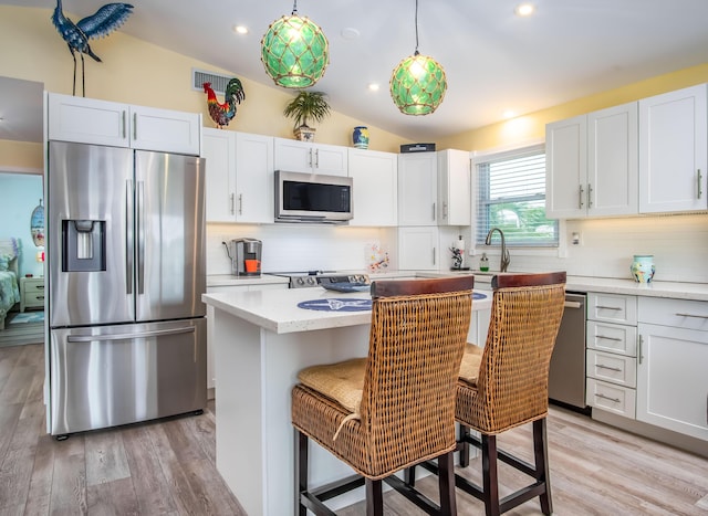 kitchen featuring a breakfast bar, appliances with stainless steel finishes, white cabinetry, hanging light fixtures, and a kitchen island