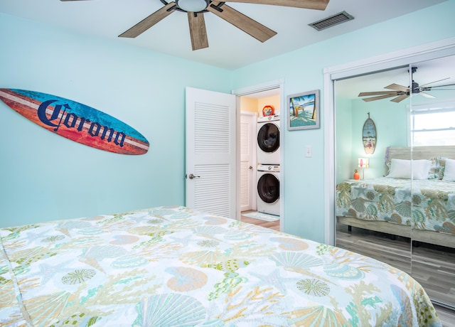 bedroom featuring stacked washer / drying machine, hardwood / wood-style flooring, a closet, and ceiling fan