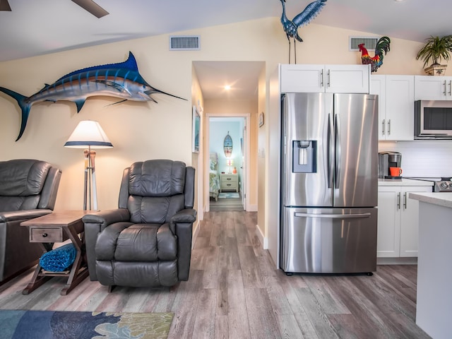 kitchen featuring lofted ceiling, white cabinetry, hardwood / wood-style floors, stainless steel appliances, and tasteful backsplash