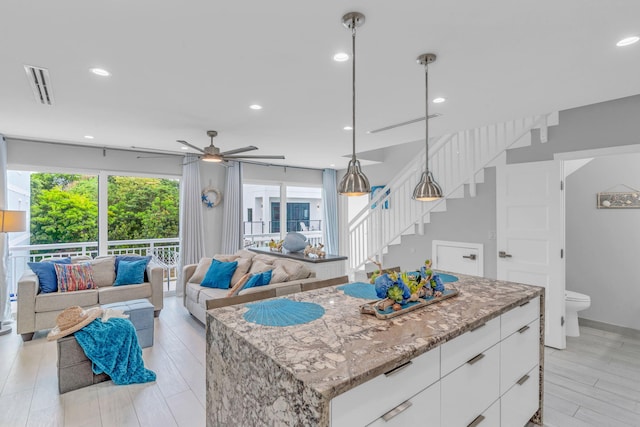 kitchen with a kitchen island, pendant lighting, white cabinetry, light stone counters, and light hardwood / wood-style flooring