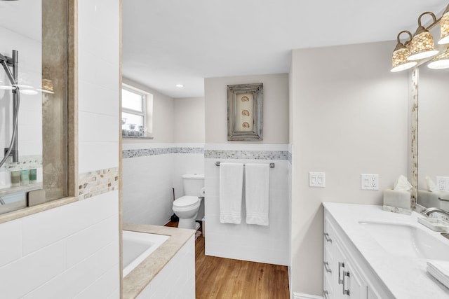 bathroom with a bathing tub, wood-type flooring, tile walls, vanity, and toilet