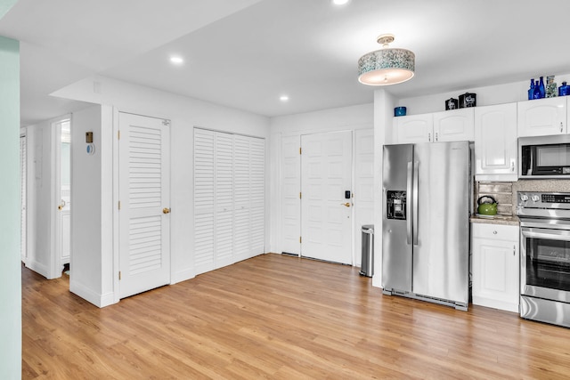 kitchen with appliances with stainless steel finishes, white cabinets, backsplash, and light hardwood / wood-style flooring