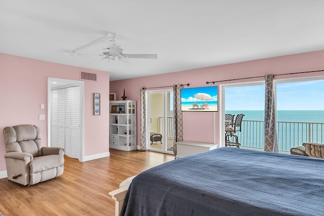 bedroom with a water view, hardwood / wood-style floors, access to exterior, and ceiling fan