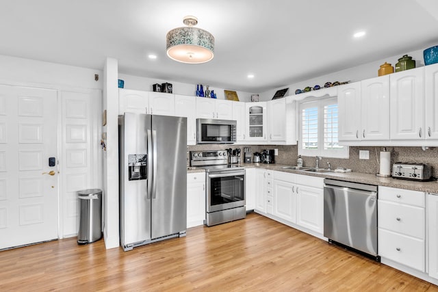 kitchen with sink, appliances with stainless steel finishes, white cabinetry, backsplash, and light hardwood / wood-style floors