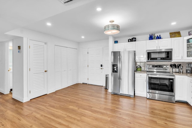 kitchen featuring tasteful backsplash, light hardwood / wood-style flooring, appliances with stainless steel finishes, light stone countertops, and white cabinets