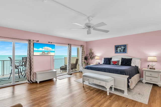 bedroom featuring multiple windows, access to exterior, light wood-type flooring, and a water view