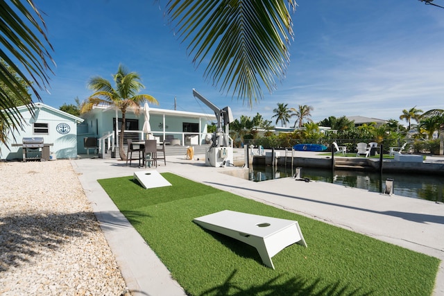 view of community featuring a water view, a dock, a patio area, and a lawn