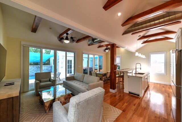 living room with lofted ceiling with beams, sink, a wealth of natural light, and light hardwood / wood-style floors