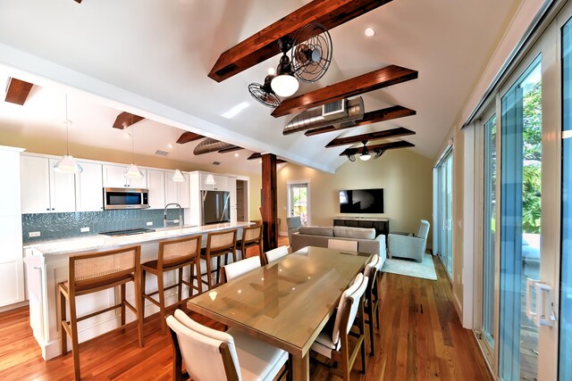 dining space with wood-type flooring, vaulted ceiling with beams, and sink