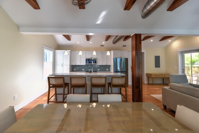 kitchen featuring a breakfast bar, appliances with stainless steel finishes, white cabinetry, lofted ceiling with beams, and decorative light fixtures