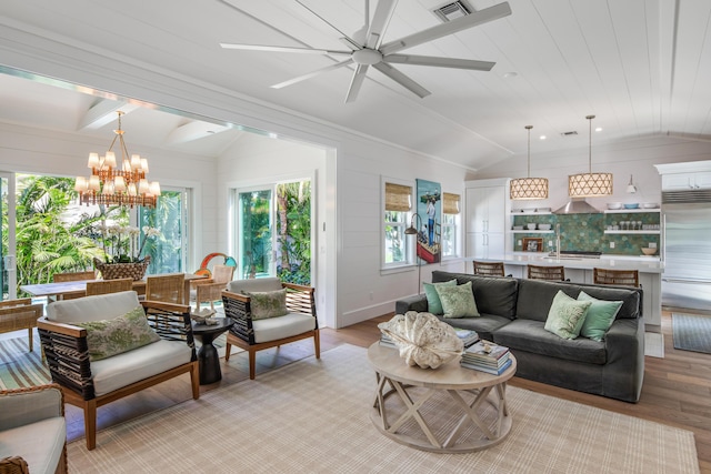 living area with vaulted ceiling, light wood-style flooring, ceiling fan with notable chandelier, and visible vents