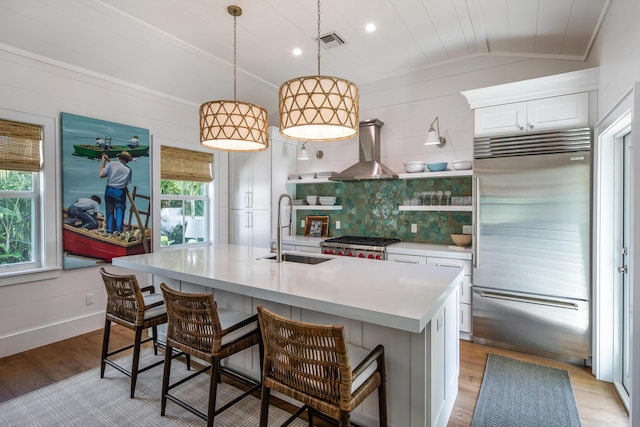 kitchen with a sink, visible vents, a healthy amount of sunlight, wall chimney range hood, and stainless steel built in fridge