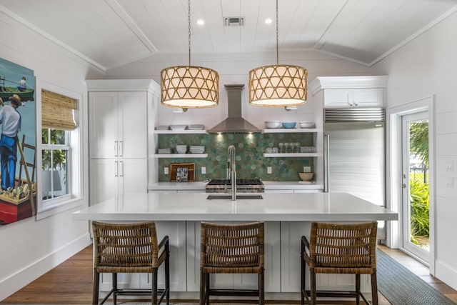 kitchen with lofted ceiling, wall chimney exhaust hood, built in refrigerator, and visible vents