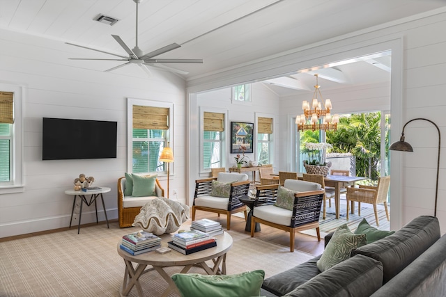 living area with light carpet, ceiling fan with notable chandelier, visible vents, baseboards, and vaulted ceiling