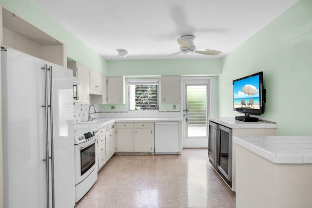 kitchen featuring appliances with stainless steel finishes, tile countertops, white cabinetry, sink, and ceiling fan