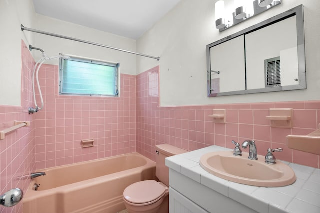 full bathroom with tiled shower / bath, tile walls, vanity, and toilet