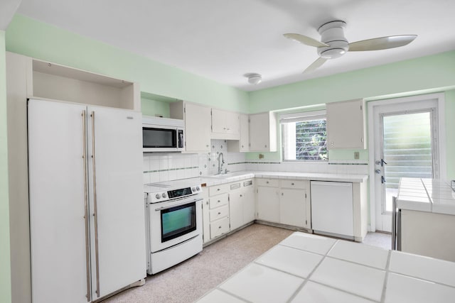 kitchen with sink, backsplash, tile counters, white appliances, and white cabinets