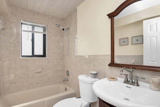 full bathroom with tiled shower / bath, vanity, toilet, and tile walls