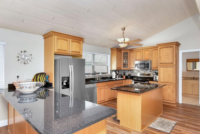 kitchen featuring stainless steel appliances, a kitchen island, light wood-type flooring, and dark stone counters