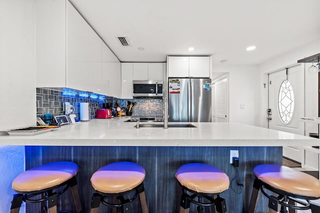 kitchen with sink, appliances with stainless steel finishes, a kitchen breakfast bar, white cabinets, and kitchen peninsula