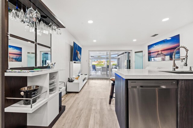 kitchen featuring stainless steel dishwasher, a kitchen breakfast bar, sink, and light hardwood / wood-style flooring