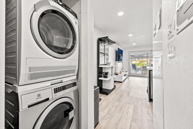 clothes washing area featuring stacked washer and clothes dryer and light wood-type flooring