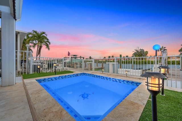 pool at dusk featuring a water view and a patio area