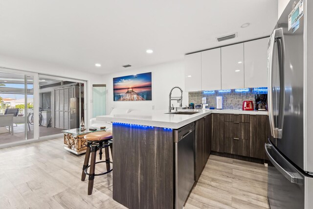 kitchen with sink, stainless steel fridge, black dishwasher, a kitchen breakfast bar, and white cabinets