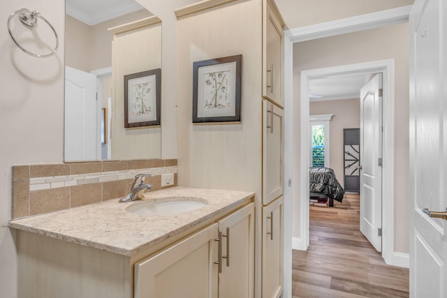 bathroom with vanity, wood finished floors, baseboards, ornamental molding, and backsplash